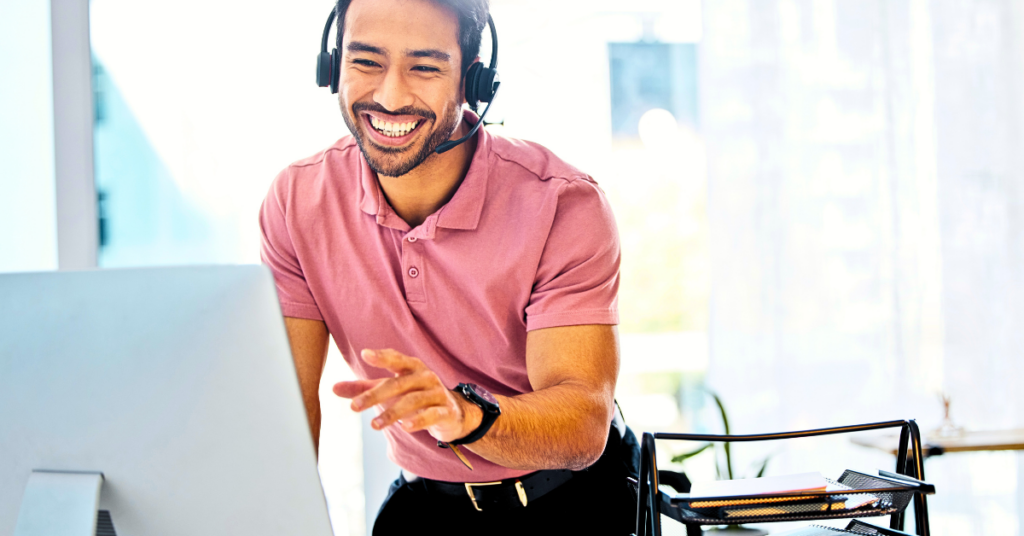 Young man smiling while talking on a headset and pointing at a screen