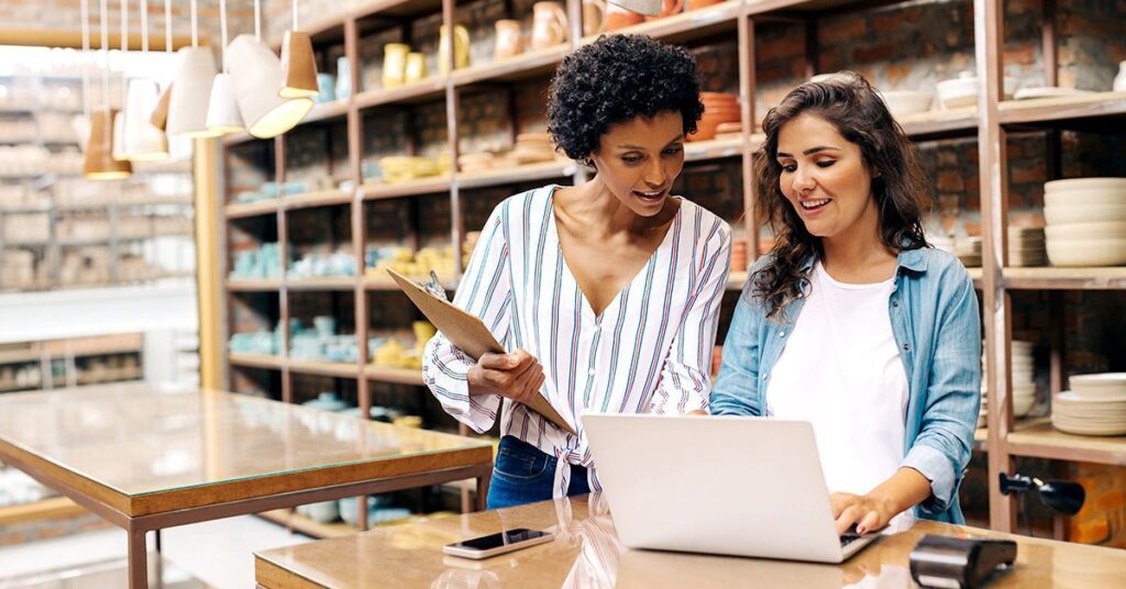 Two women looking at a laptop screen in a pottery store